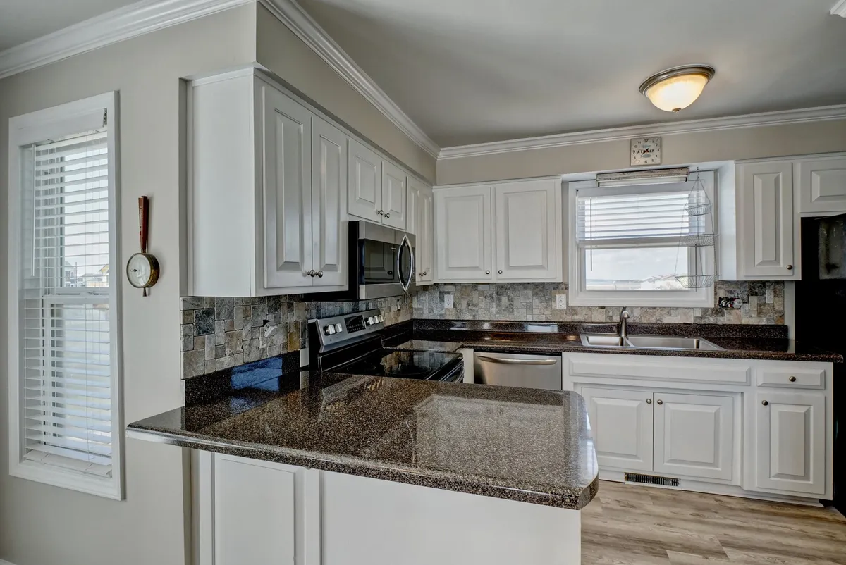 A bright, welcoming kitchen featuring granite countertops, white cabinetry, stainless steel appliances, and a window that fills the space with natural light. The setup is inviting for meal prep and family gatherings, emphasizing practical amenities.