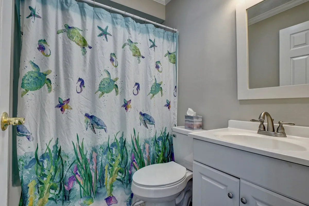 A playful, coastal-themed bathroom with a colorful shower curtain covered in marine life motifs, a white vanity and sink, and a simple mirror. The design is bright and family-friendly, making daily routines more enjoyable.