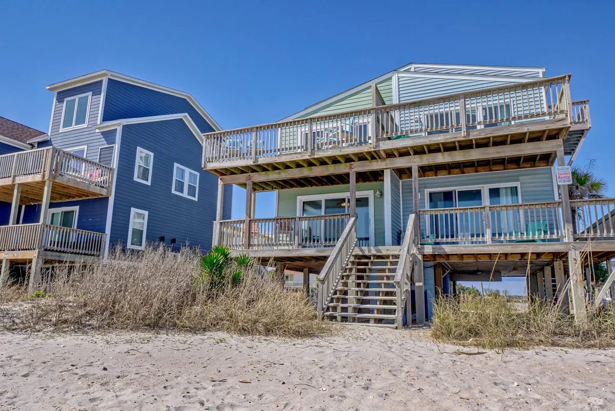 A beachfront property with a spacious wooden deck and stairs leading directly onto the sand. The deck is ideal for lounging, gathering with family, or enjoying meals while overlooking the ocean.