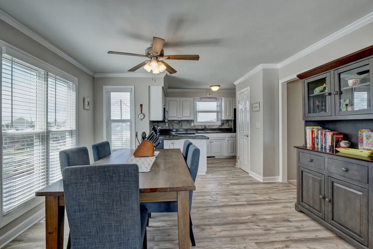 A bright dining area flows into a fully equipped kitchen, with windows letting in abundant light. The dining table is set for family meals or festivities, and the kitchen is complete with modern amenities, creating a functional space for preparing and sharing meals.
