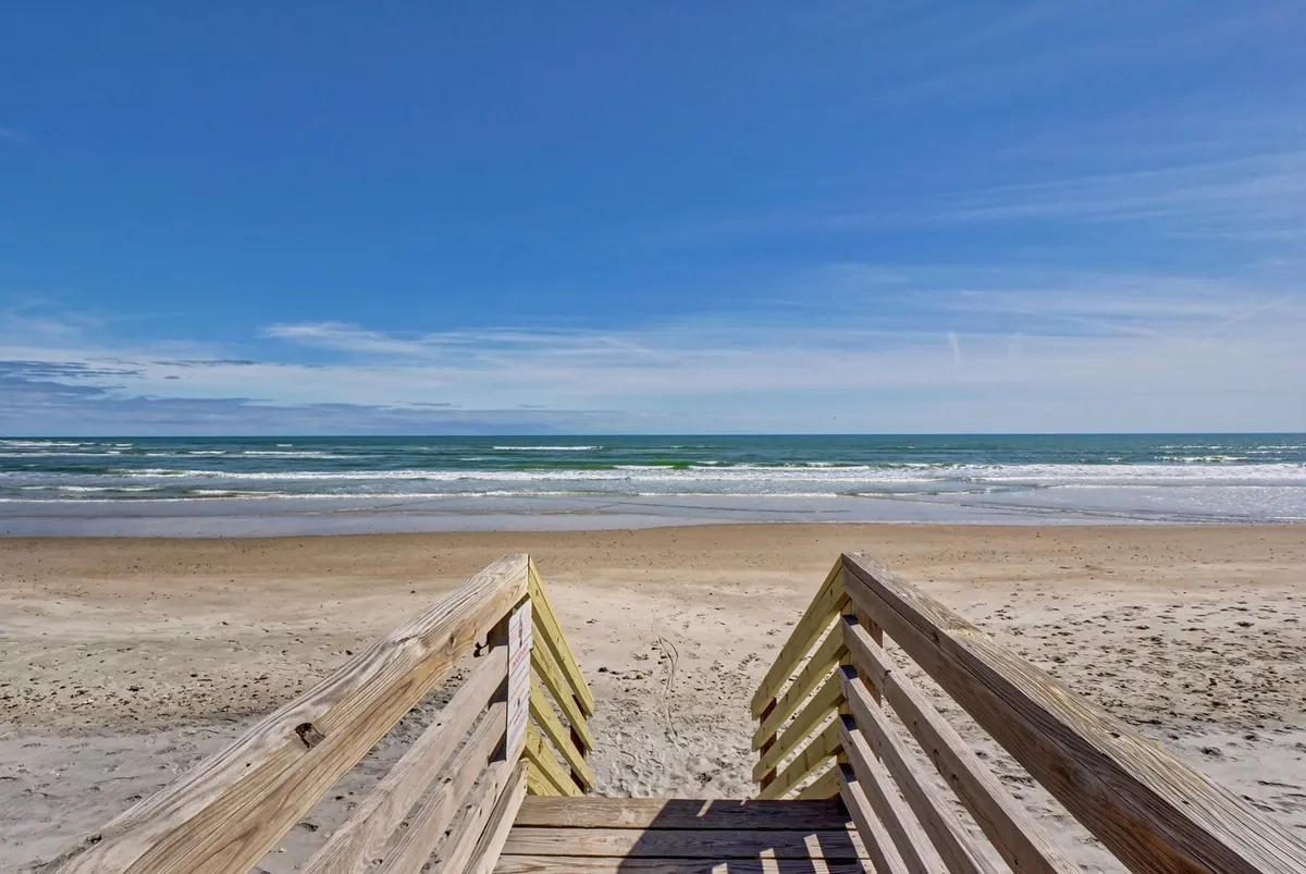 Wooden stairs leading down from the property to the beach, with an open view of the ocean and expansive sky. The image captures the seamless connection between the home and the waterfront, emphasizing easy beach access.