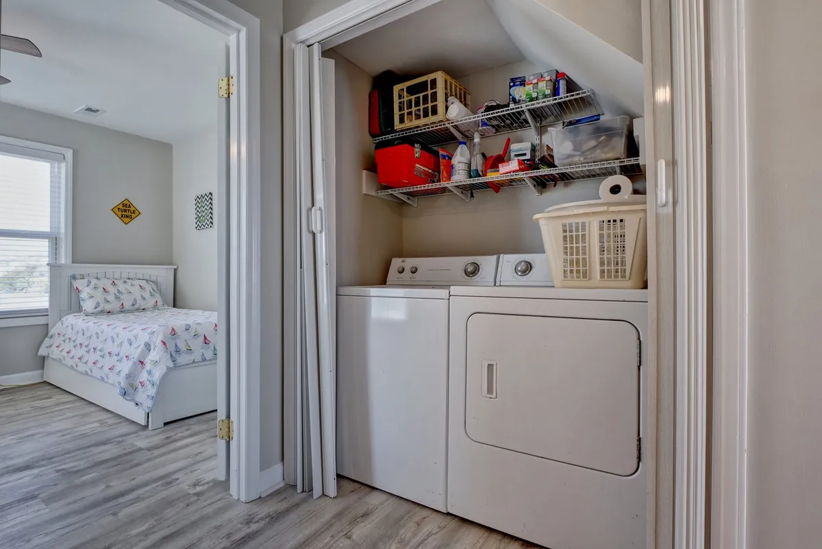 A tidy laundry area featuring a modern washing machine and dryer, with storage baskets neatly arranged for convenience. The space is well-lit and situated next to a cozy bedroom, blending practicality with comfort, indicating easy laundry access for guests during their stay.