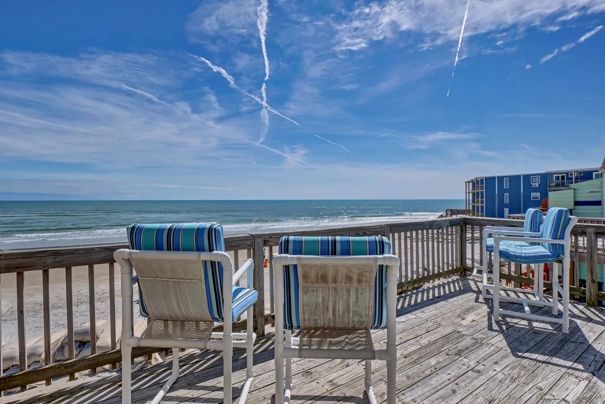 A tranquil private deck overlooks the ocean, furnished with deck chairs for relaxing, socializing, or enjoying morning coffee and sunset toasts. The blue sky and expansive sea complete the inviting scene.